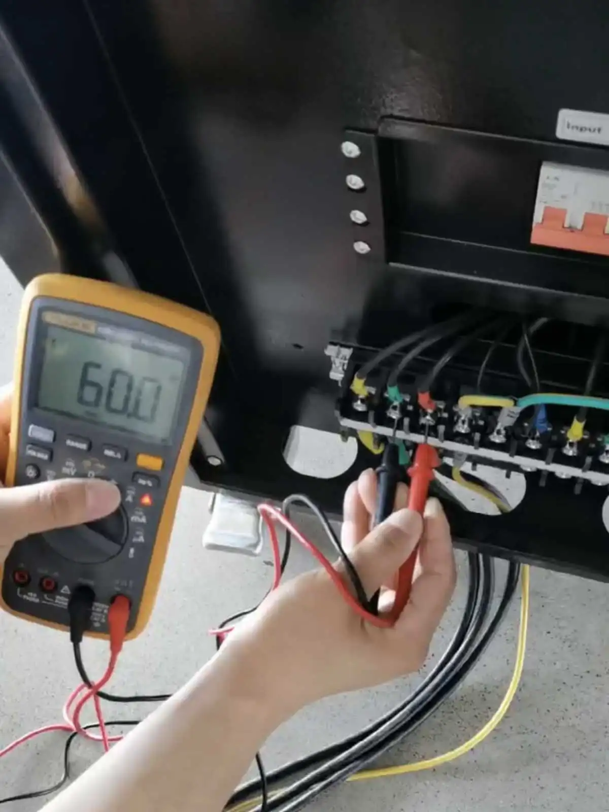 Handheld meter measuring 60.0Hz at the WVFP-33020 input terminals during factory testing.
